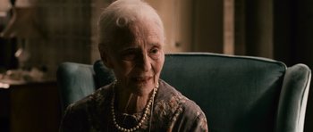 Movie still from “Knowing” (2009), directed by Alex Proyas – An older woman with a necklace sitting in a chair; Close Up shot, Over the shoulder angle