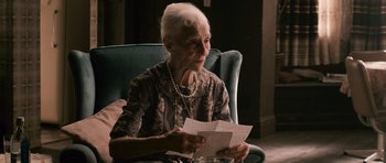 Movie still from “Knowing” (2009), directed by Alex Proyas – An older woman sitting in a chair looking at a piece of paper; Close Up shot, Over the shoulder angle