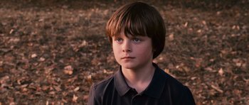 Movie still from “Knowing” (2009), directed by Alex Proyas – A young boy with blue eyes is standing in a field; Close Up shot, High angle