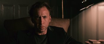 Movie still from “Knowing” (2009), directed by Alex Proyas – A person sitting in a chair wearing a jacket; Close Up shot, Low angle