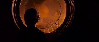 Movie still from “Knowing” (2009), directed by Alex Proyas – A woman looking out a window at a fire; Medium shot, Over the shoulder angle