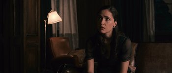 Movie still from “Knowing” (2009), directed by Alex Proyas – A woman sitting on a chair in a dark room; Medium shot, Over the shoulder angle