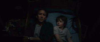 Movie still from “Knowing” (2009), directed by Alex Proyas – A man and a boy laying in bed next to each other; Medium shot, High angle