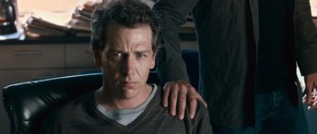 Movie still from “Knowing” (2009), directed by Alex Proyas – A man standing next to another man with his arms around another man; Close Up shot, Over the shoulder angle
