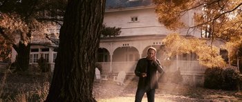 Movie still from “Knowing” (2009), directed by Alex Proyas – A man standing in front of a house on a cell phone; Medium shot, Low angle