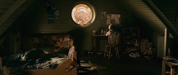 Movie still from “Knowing” (2009), directed by Alex Proyas – A person sitting at a desk in front of a round window; Extreme Wide shot, High angle