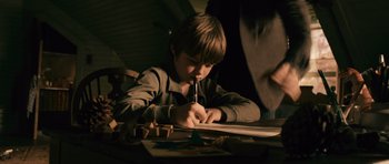 Movie still from “Knowing” (2009), directed by Alex Proyas – A young boy writing on a piece of paper; Medium shot, High angle