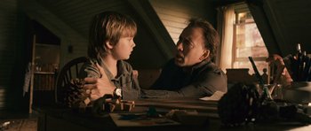 Movie still from “Knowing” (2009), directed by Alex Proyas – A man and a boy sitting at a wooden table; Medium shot, Over the shoulder angle