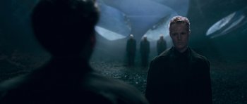 Movie still from “Knowing” (2009), directed by Alex Proyas – A group of people standing in a dark room; Medium shot, Over the shoulder angle