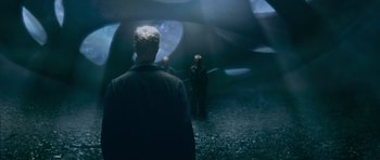 Movie still from “Knowing” (2009), directed by Alex Proyas – Two men standing next to each other in the dark; Wide shot, Over the shoulder angle