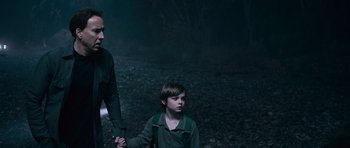 Movie still from “Knowing” (2009), directed by Alex Proyas – A man and a boy holding hands in a dark forest; Medium shot, Over the shoulder angle