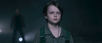 Movie still from “Knowing” (2009), directed by Alex Proyas – A young boy wearing a green shirt and black shirt; Close Up shot, Low angle