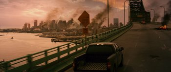 Movie still from “Knowing” (2009), directed by Alex Proyas – A truck driving down a bridge with a city in the background; Extreme Wide shot, High angle