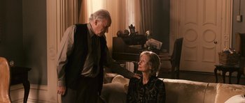 Movie still from “Knowing” (2009), directed by Alex Proyas – An older man touching the shoulder of a woman; Medium shot, Over the shoulder angle