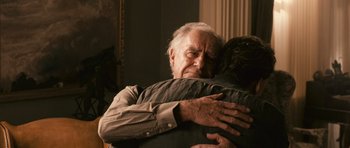 Movie still from “Knowing” (2009), directed by Alex Proyas – An older man hugging a younger man in a living room; Close Up shot, Over the shoulder angle