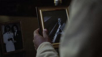 Movie still from “Atlanta” (2016), created by Donald Glover – A person holding a picture of a man playing a piano; Extreme Close Up shot, High angle