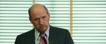 Movie still from “Kong: Skull Island” (2017), directed by Jordan Vogt-Roberts – An older man wearing a suit and tie; Close Up shot, Over the shoulder angle