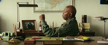Movie still from “Kong: Skull Island” (2017), directed by Jordan Vogt-Roberts – A man sitting at a desk in front of a map; Medium shot, Over the shoulder angle