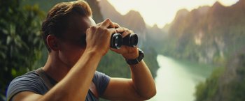 Movie still from “Kong: Skull Island” (2017), directed by Jordan Vogt-Roberts – A man looking through a pair of binoculars; Close Up shot, Over the shoulder angle