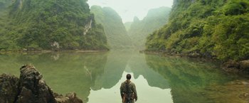 Movie still from “Kong: Skull Island” (2017), directed by Jordan Vogt-Roberts – A man standing on the edge of a lake looking out at the mountains; Extreme Wide shot, Low angle