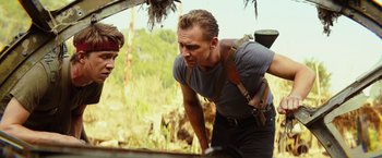 Movie still from “Kong: Skull Island” (2017), directed by Jordan Vogt-Roberts – A man standing next to another man on a field; Medium shot, Over the shoulder angle