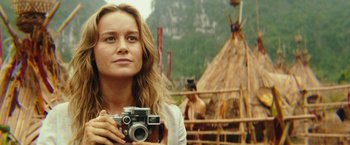 Movie still from “Kong: Skull Island” (2017), directed by Jordan Vogt-Roberts – A woman holding a camera in front of a teepee; Close Up shot, Over the shoulder angle