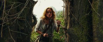 Movie still from “Kong: Skull Island” (2017), directed by Jordan Vogt-Roberts – A woman with a camera standing next to a tree; Medium shot, Low angle