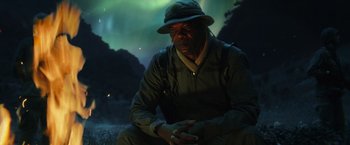 Movie still from “Kong: Skull Island” (2017), directed by Jordan Vogt-Roberts – A man sitting on the ground in front of a sky filled with green lights; Medium shot, Low angle
