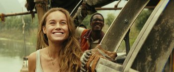 Movie still from “Kong: Skull Island” (2017), directed by Jordan Vogt-Roberts – A woman smiling while holding a large wooden object; Close Up shot, Low angle
