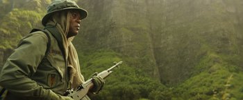 Movie still from “Kong: Skull Island” (2017), directed by Jordan Vogt-Roberts – A man holding a rifle while standing in front of a mountain; Close Up shot, Low angle