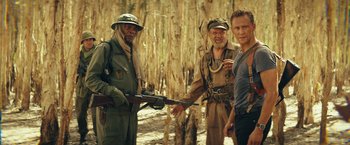 Movie still from “Kong: Skull Island” (2017), directed by Jordan Vogt-Roberts – A group of men standing next to each other in the woods; Medium shot, Over the shoulder angle