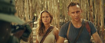 Movie still from “Kong: Skull Island” (2017), directed by Jordan Vogt-Roberts – A man and a woman standing next to each other in the woods; Medium shot, Over the shoulder angle