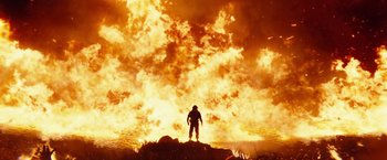 Movie still from “Kong: Skull Island” (2017), directed by Jordan Vogt-Roberts – A person standing on top of a rock in front of a fire; Wide shot, Low angle