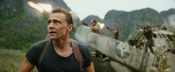 Movie still from “Kong: Skull Island” (2017), directed by Jordan Vogt-Roberts – A man standing in front of an airplane with other men in the background; Medium shot, Over the shoulder angle