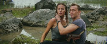 Movie still from “Kong: Skull Island” (2017), directed by Jordan Vogt-Roberts – A man and a woman sitting next to each other in the grass; Medium shot, Over the shoulder angle
