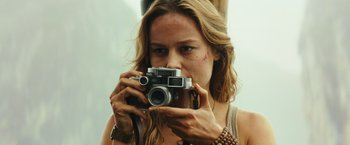 Movie still from “Kong: Skull Island” (2017), directed by Jordan Vogt-Roberts – A woman taking a picture with a camera; Close Up shot, Low angle