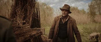 Movie still from “Lamborghini: The Man Behind the Legend” (2022), directed by Bobby Moresco – A man in a hat standing next to a wooden fence; Medium shot, Over the shoulder angle