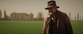 Movie still from “Lamborghini: The Man Behind the Legend” (2022), directed by Bobby Moresco – An older man in a hat and a jacket in front of a field; Medium shot, Low angle