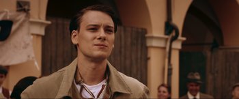 Movie still from “Lamborghini: The Man Behind the Legend” (2022), directed by Bobby Moresco – A young man wearing a tan jacket and a white shirt; Close Up shot, Over the shoulder angle