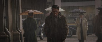 Movie still from “Lamborghini: The Man Behind the Legend” (2022), directed by Bobby Moresco – A man smoking a cigarette while standing in the pouring rain; Medium shot, Low angle
