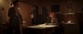 Movie still from “Lamborghini: The Man Behind the Legend” (2022), directed by Bobby Moresco – A woman sitting at a table in a dimly - lit room; Wide shot, Over the shoulder angle