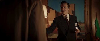 Movie still from “Lamborghini: The Man Behind the Legend” (2022), directed by Bobby Moresco – A man wearing a suit and tie standing in front of a mirror; Medium shot, Over the shoulder angle