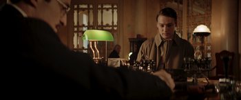 Movie still from “Lamborghini: The Man Behind the Legend” (2022), directed by Bobby Moresco – A man sitting in front of a green lamp in a room; Medium shot, Over the shoulder angle