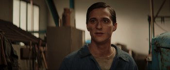 Movie still from “Lamborghini: The Man Behind the Legend” (2022), directed by Bobby Moresco – A young man in a blue shirt is looking at the camera; Close Up shot, Over the shoulder angle