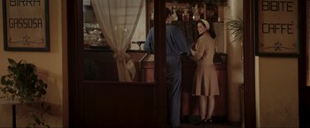 Movie still from “Lamborghini: The Man Behind the Legend” (2022), directed by Bobby Moresco – A woman standing at a counter in a restaurant; Medium shot, Over the shoulder angle