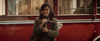 Movie still from “Lamborghini: The Man Behind the Legend” (2022), directed by Bobby Moresco – A woman in a brown coat holding a book and a purse; Medium shot, Over the shoulder angle