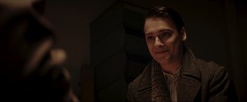 Movie still from “Lamborghini: The Man Behind the Legend” (2022), directed by Bobby Moresco – A young man wearing a brown jacket and a brown scarf; Close Up shot, Over the shoulder angle