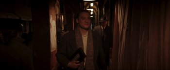 Movie still from “Lamborghini: The Man Behind the Legend” (2022), directed by Bobby Moresco – A man in a suit and tie holding a book in a hallway; Medium shot, Low angle