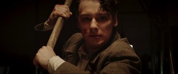 Movie still from “Lamborghini: The Man Behind the Legend” (2022), directed by Bobby Moresco – A young man holding a baseball bat in a room; Close Up shot, Low angle