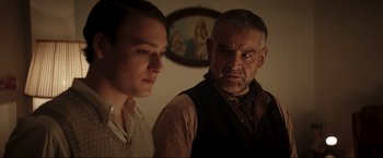 Movie still from “Lamborghini: The Man Behind the Legend” (2022), directed by Bobby Moresco – A man standing next to a woman in front of a painting; Medium shot, Over the shoulder angle